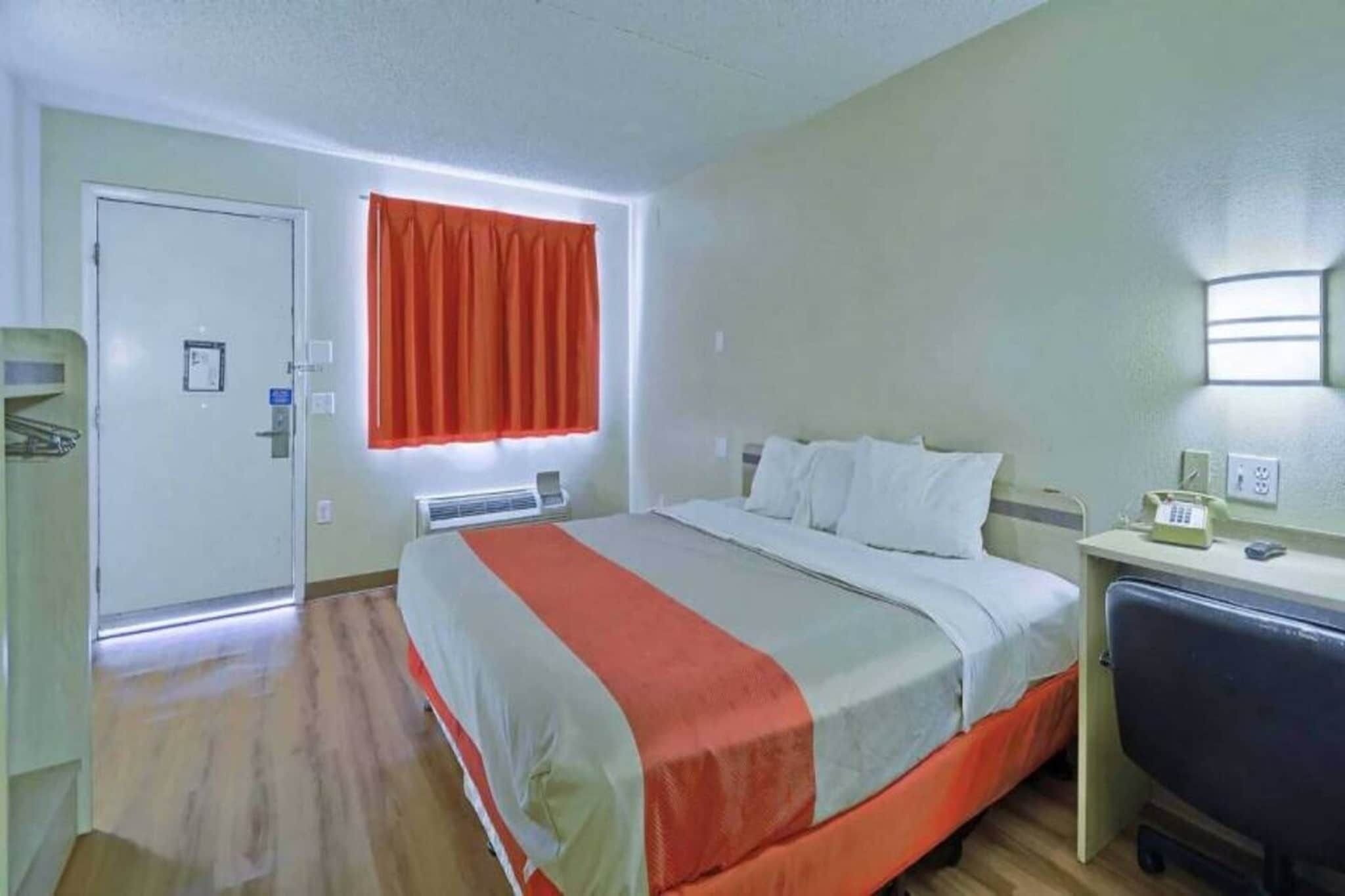 Een hotelkamer met een bed, een bureau, een stoel, een raam met gordijnen en een deur.