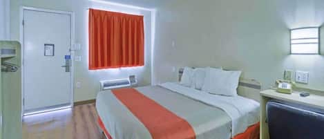 A hotel room with a bed, a desk, a chair, a window with curtains, and a door.