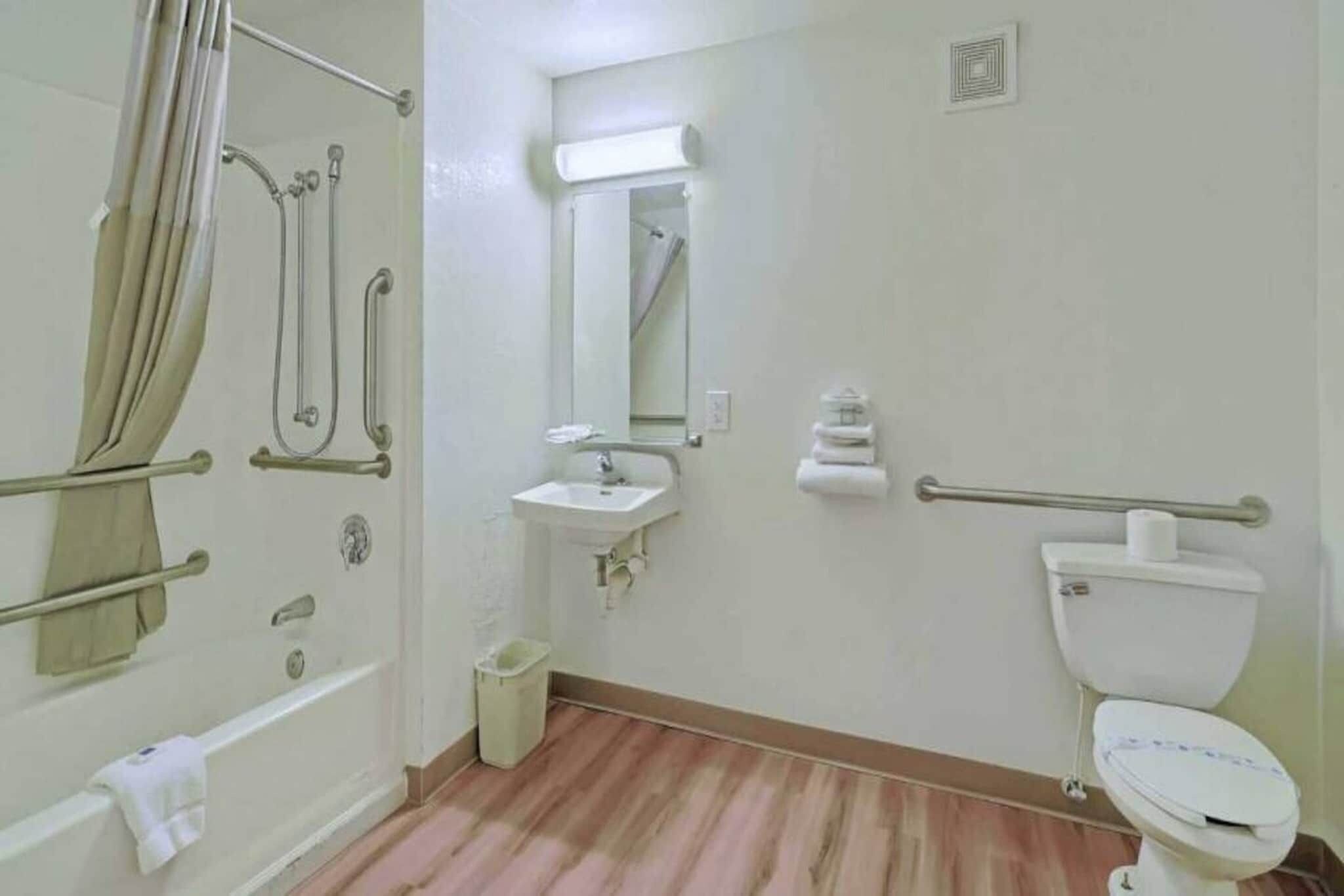 Ein Badezimmer mit Dusche, Waschbecken, Toilette und Haltegriffen.