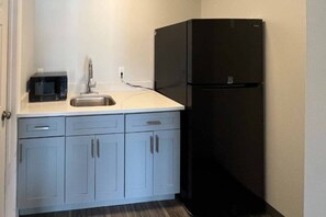 A compact kitchen with a microwave, sink, and black refrigerator.
