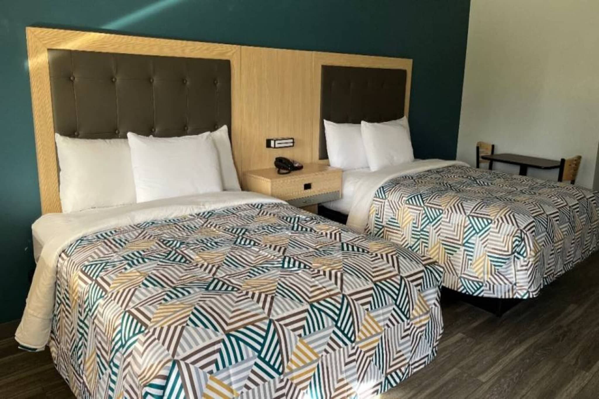Een tweepersoonskamer met twee bedden, elk voorzien van beddengoed met een patroon, een houten hoofdbord en een nachtkastje met een lamp.