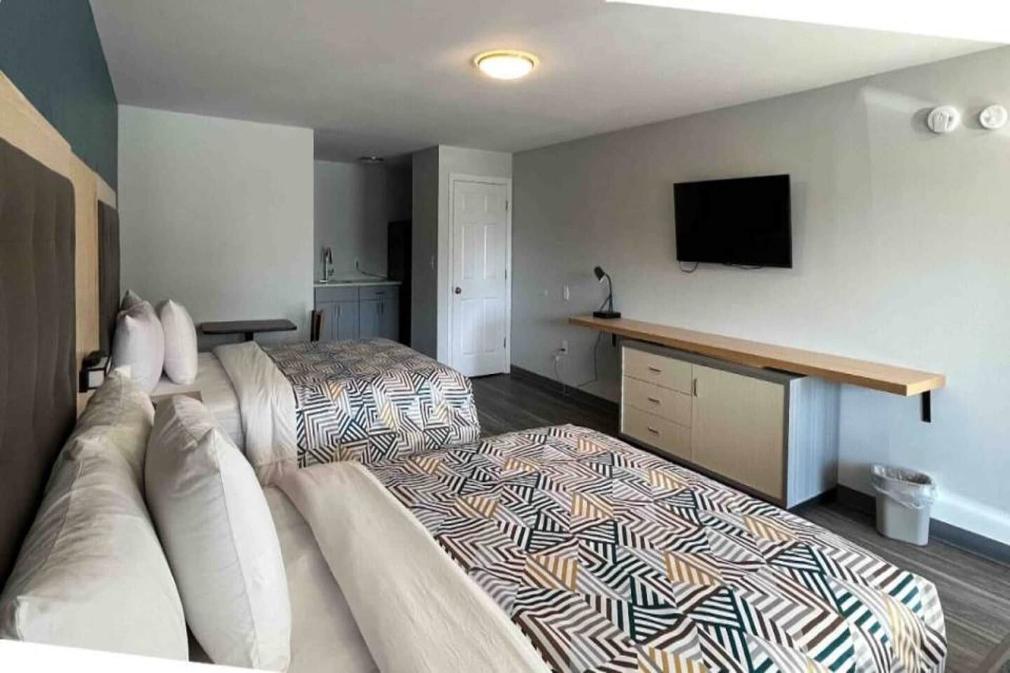 Una habitació amb dos llits, un escriptori, una televisió i una porta que dona a un bany.