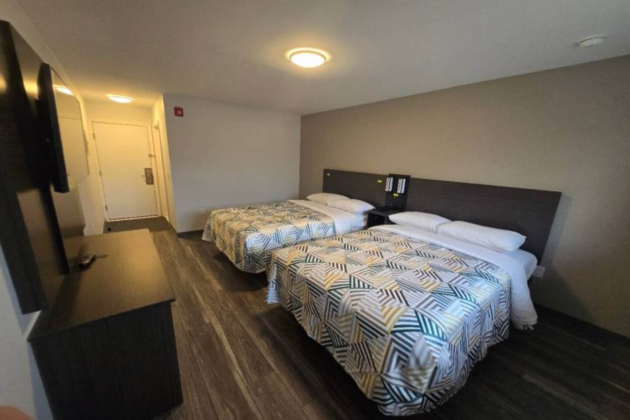 A hotel room with two beds, a TV, and a wooden floor.