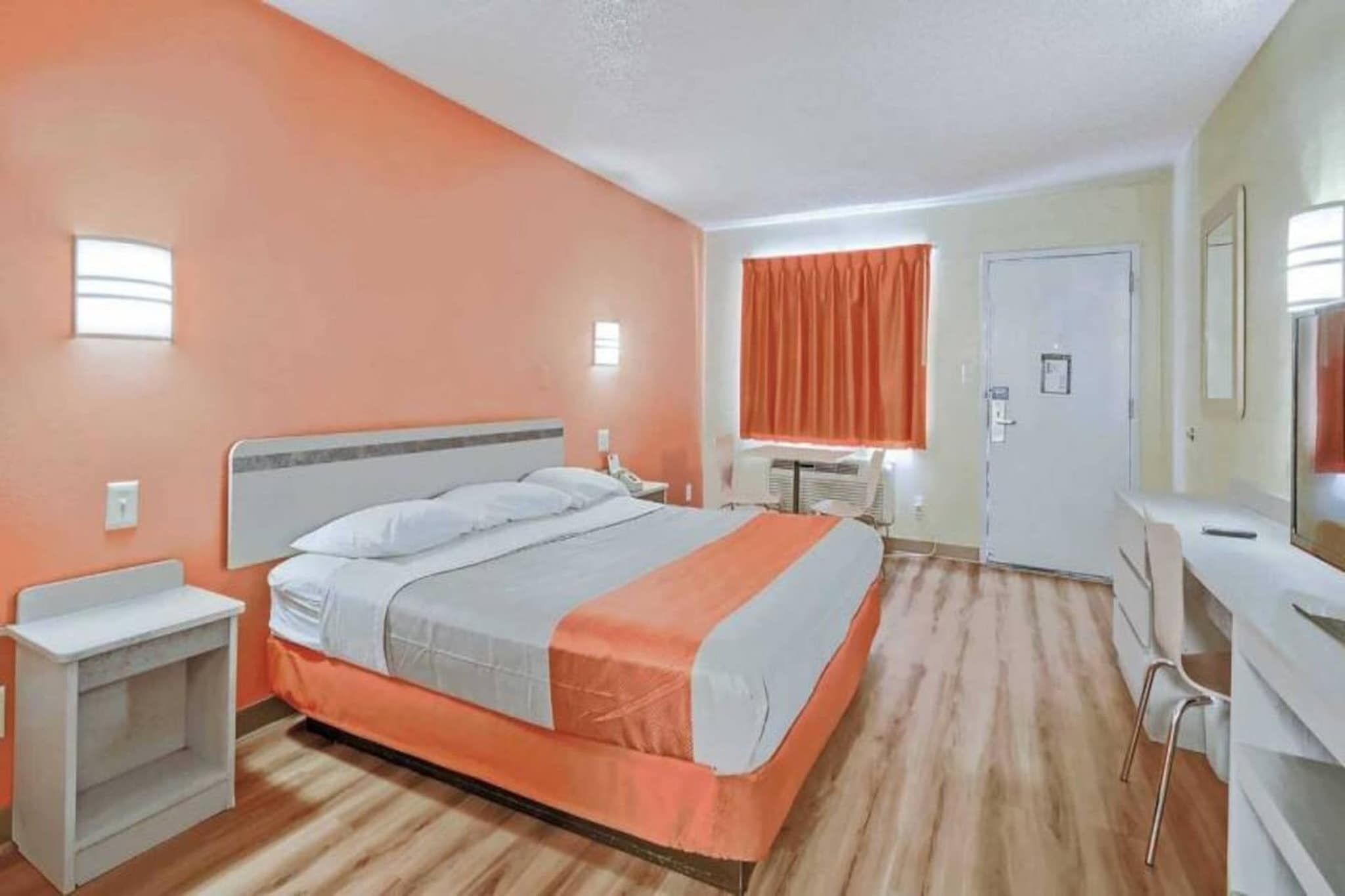 Ein Hotelzimmer mit Bett, Nachttisch, Schreibtisch, Stuhl und einem Fenster mit Vorhängen.