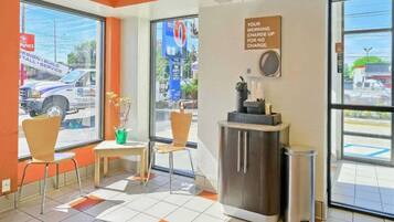A hotel lobby with a reception desk, chairs, a trash bin, and large windows offering a view of the street.