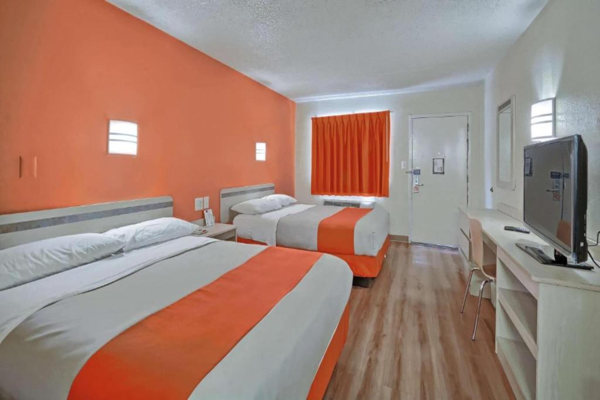 Een hotelkamer met twee bedden, een televisie en een raam met gordijnen.