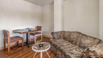Una habitación con piso de madera, un sofá estampado, una mesita redonda y una mesa de comedor con sillas.