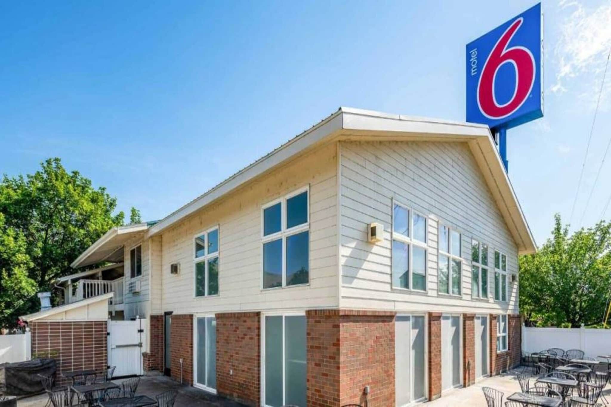 A motel with a single-story structure, a prominent '6' sign, and a patio area with outdoor seating.