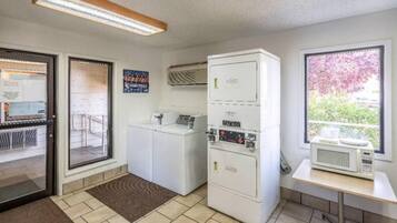A laundry room with a washing machine, dryer, and microwave. There are two doors, one leading to a balcony with a view of trees.
