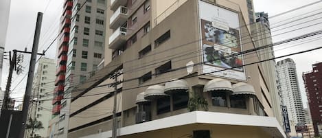 A multi-story building with balconies, a sign indicating a hotel, and parked cars on the street.