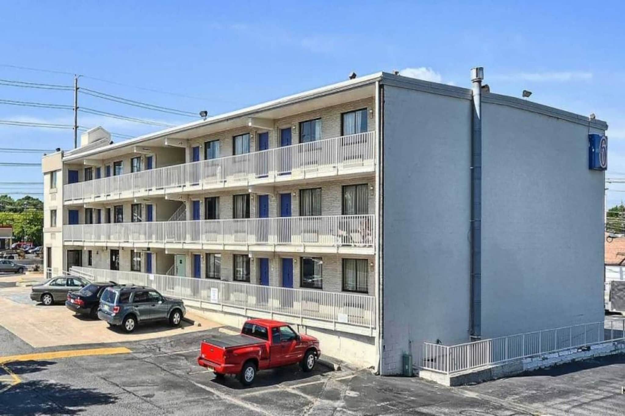 A multi-story motel with balconies, a parking lot, and a clear sky.