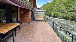 A wooden building with a terrace overlooking a river, a table and chairs, and a sign reading 'Tuvá vila bungalô'.