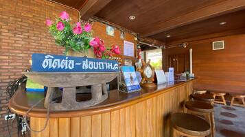 A wooden reception desk with a sign in a foreign script, a clock, and a flower arrangement.