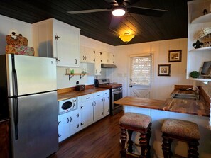 A compact kitchen with white cabinets, a built-in oven, a microwave, and a refrigerator. There are wooden stools and a wooden countertop.