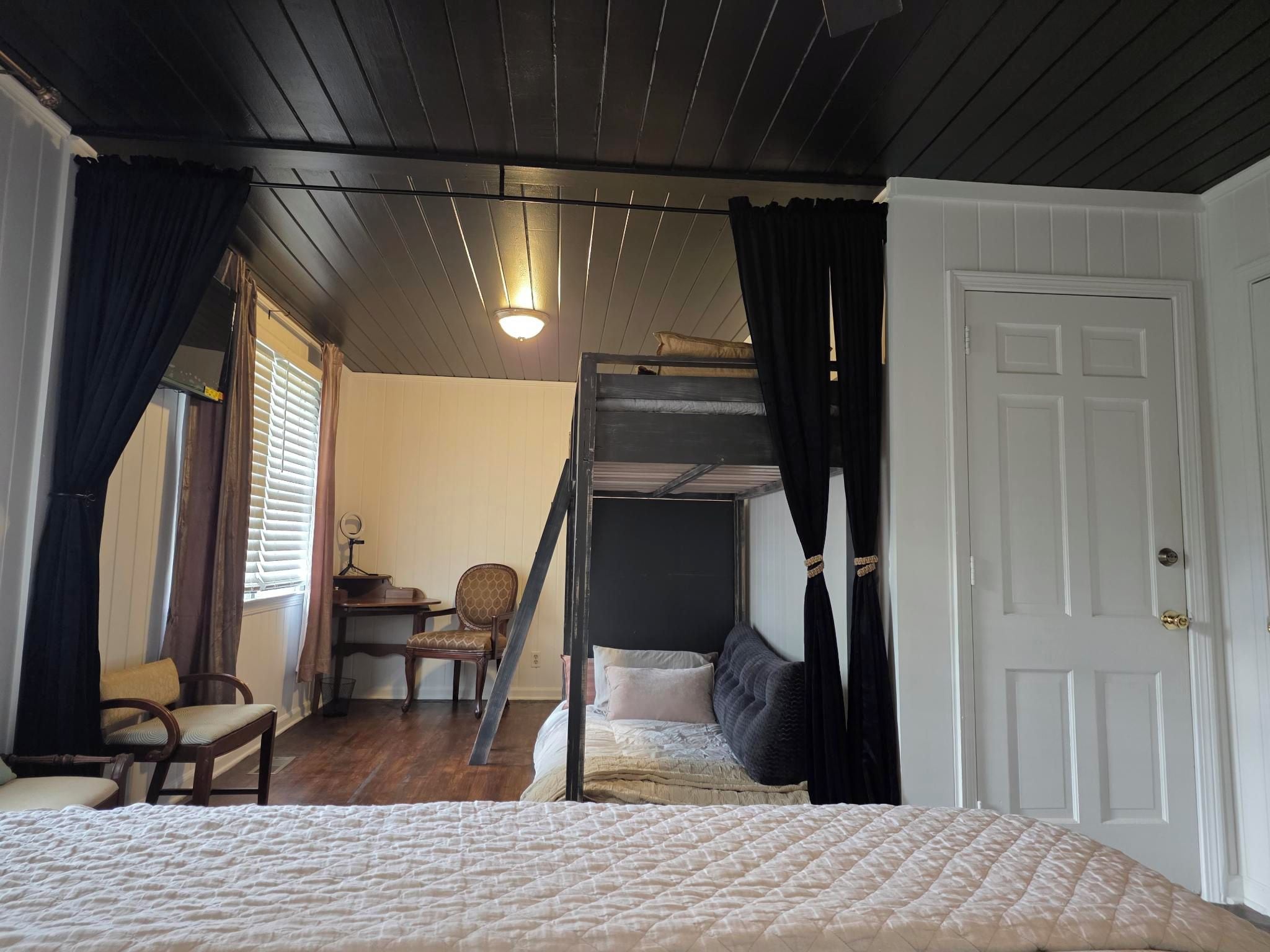A bedroom with a bunk bed, a desk with a chair, a window with curtains, and a door.