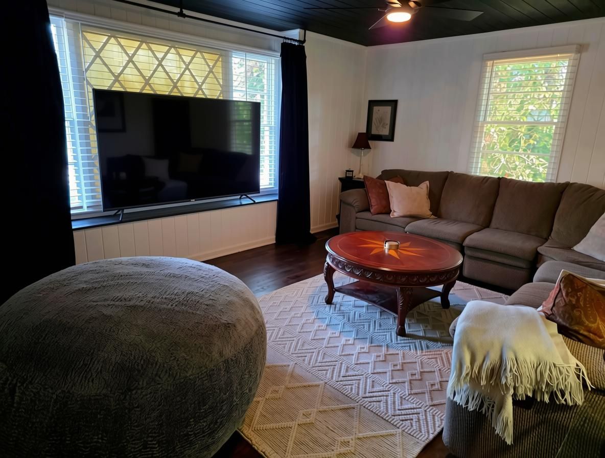 A living room with a large flat-screen TV, a sofa, a round coffee table, and a patterned rug.