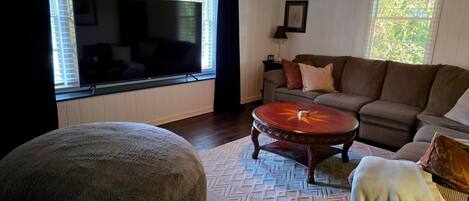 A living room with a large flat-screen TV, a sofa, a round coffee table, and a patterned rug.