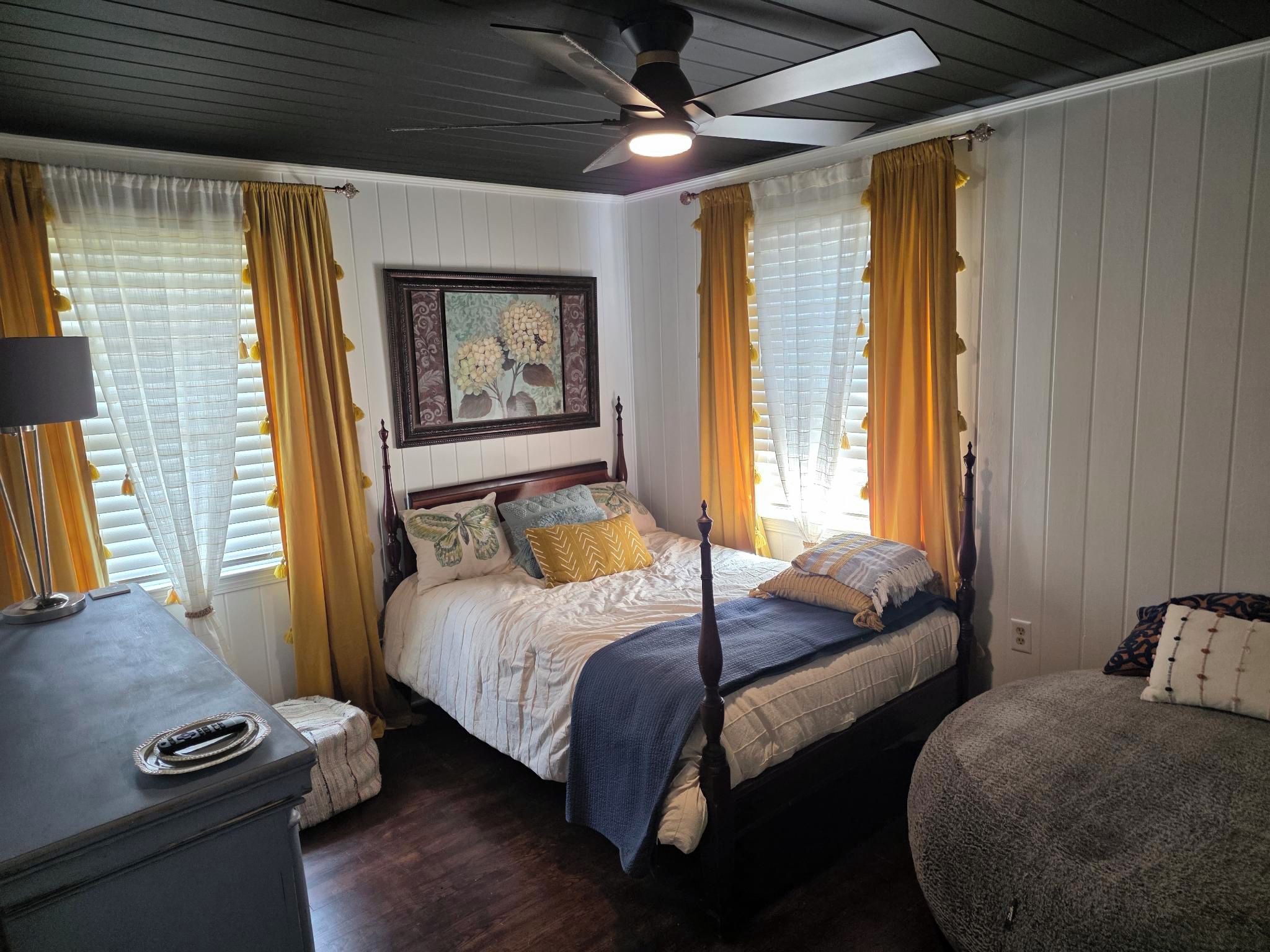 Un dormitorio con cama con dosel, ventilador de techo y un cuadro en la pared.