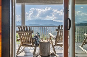 A wooden deck with two Adirondack chairs, a small round table, and a view of mountains. - Smoky Mountain View | Pickleball | Family Retreat (Gatlinburg)