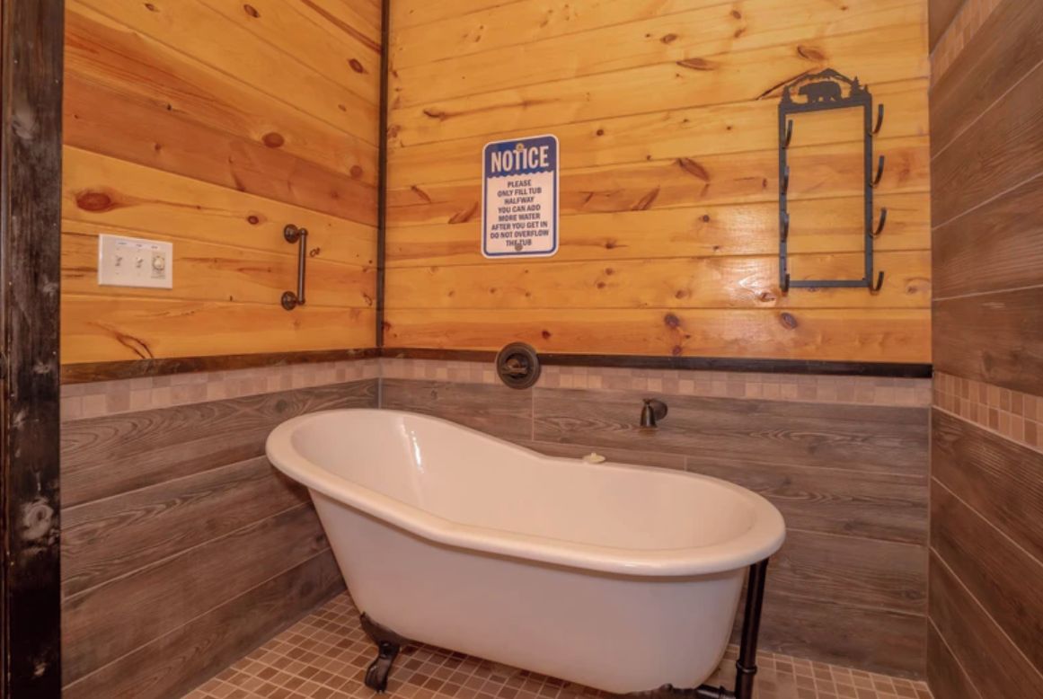 Une salle de bain avec une baignoire sur pieds, des murs en bois et un panneau d’information.