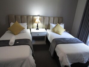 Een hotelkamer met twee eenpersoonsbedden, een nachtkastje met een lamp en een klein lade.