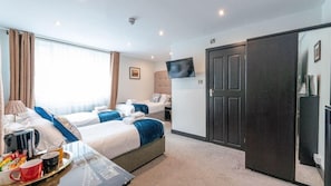 A hotel room with two beds, a flat-screen TV, a wardrobe, and a desk with a tray of breakfast items.
