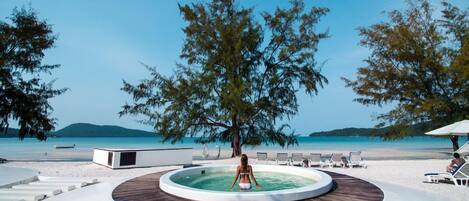 A pool area with a circular wooden deck, a person in the pool, and beach chairs and umbrellas.
