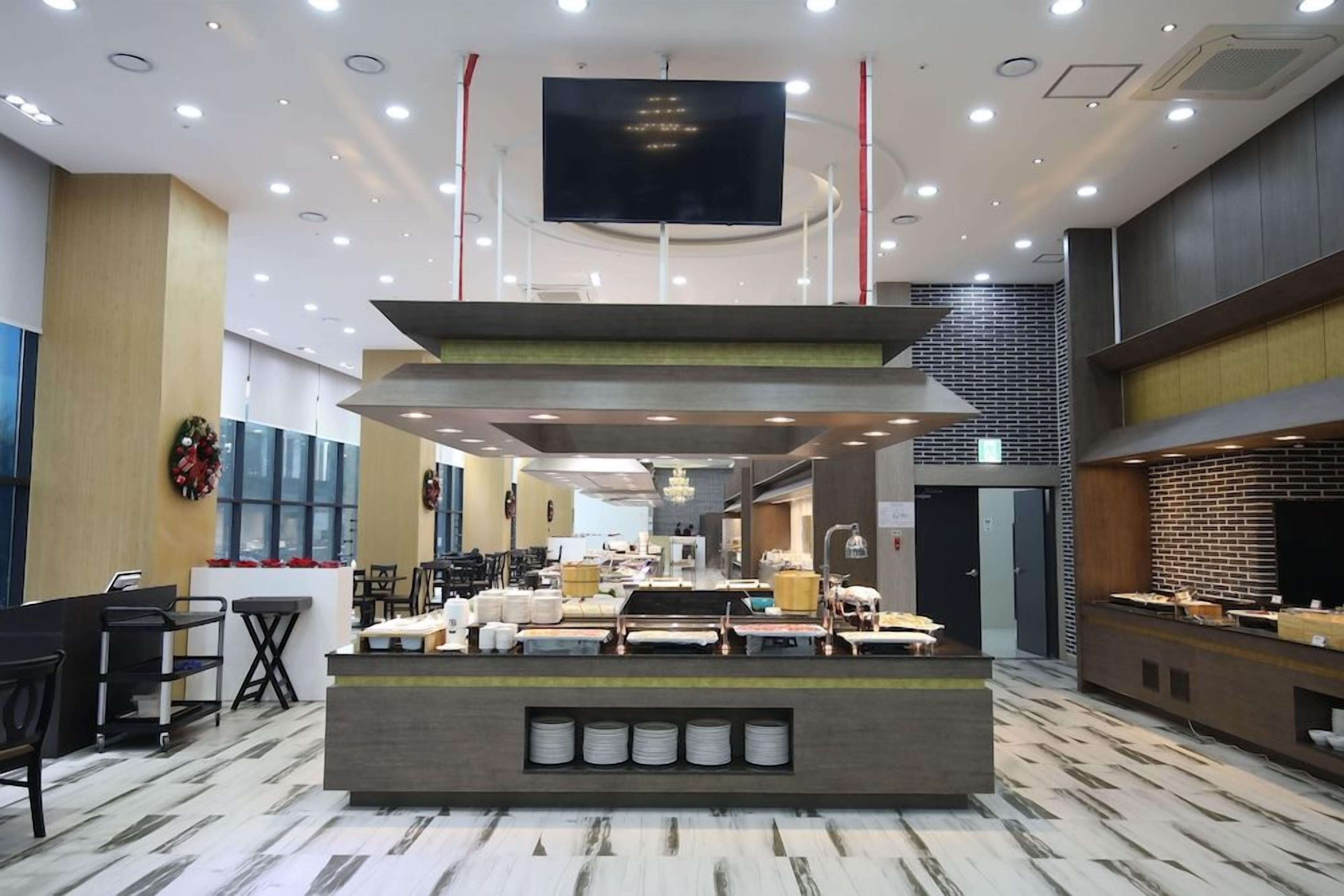 A hotel lobby with a reception desk, seating area, and a large flat-screen TV mounted on the ceiling.
