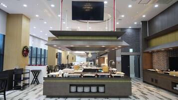 A hotel lobby with a reception desk, seating area, and a large flat-screen TV mounted on the ceiling.