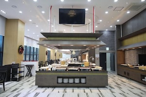 Un vestíbulo de hotel con una recepción, zona de estar y un televisor de pantalla plana grande montado en el techo.