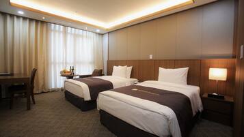 A hotel room with two beds, a desk, a chair, and a table with a fruit bowl and bottles.