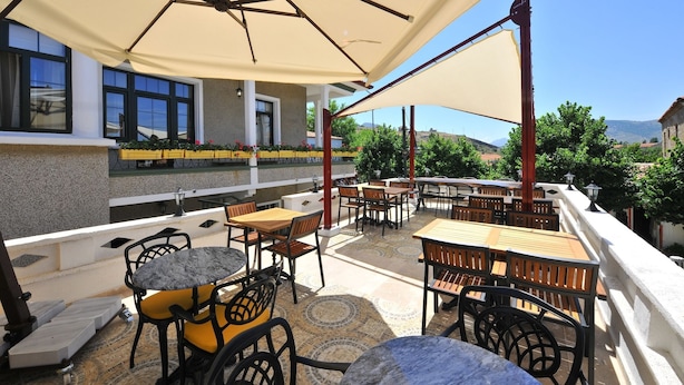 An outdoor patio with multiple tables and chairs, a pergola structure, and a view of the landscape. - Petrino Gokceada Hotel (Gökçeada)