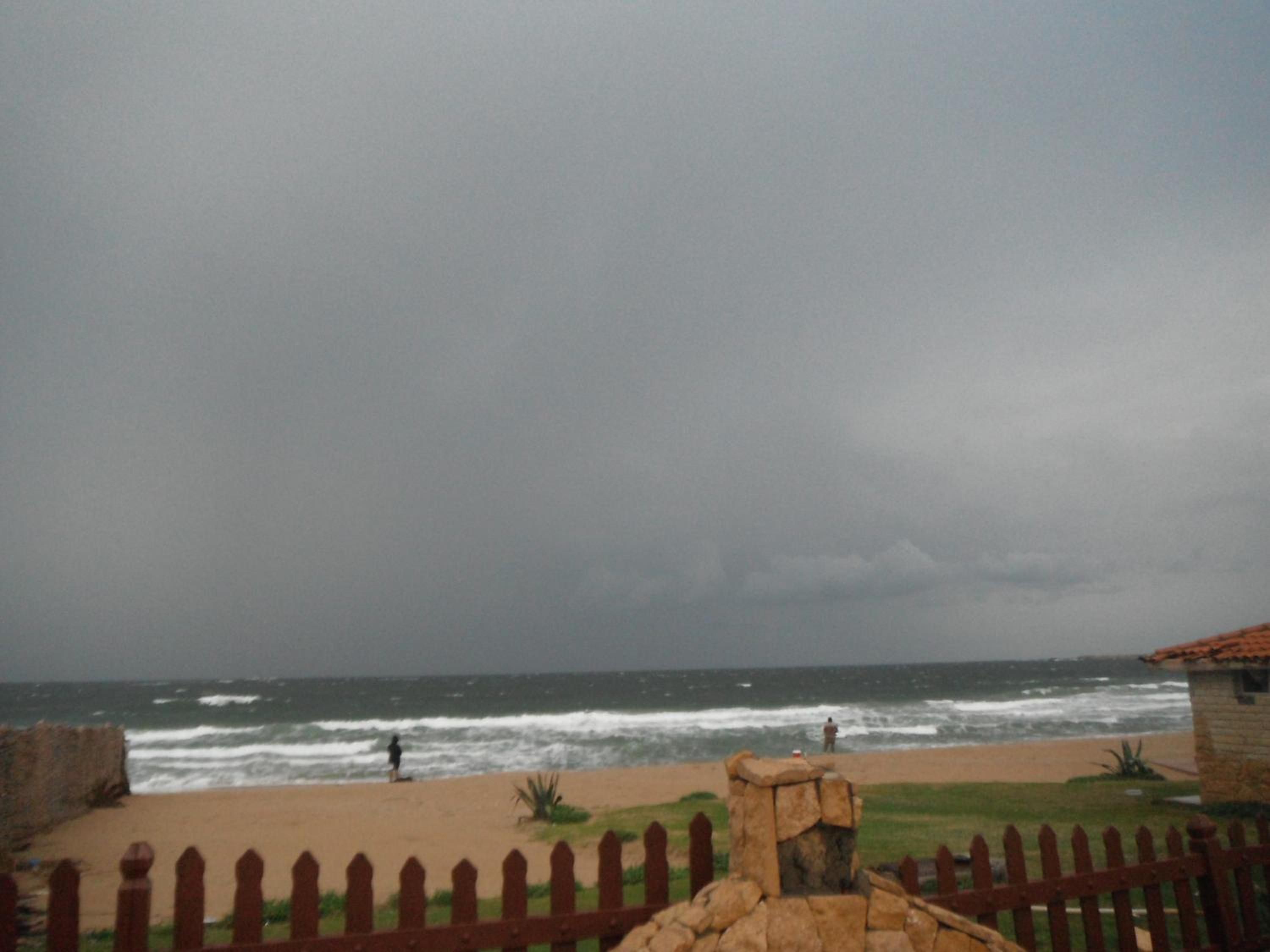 A beach with a stone wall and a wooden fence in the foreground.