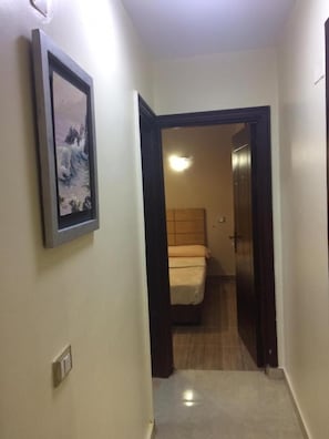 Un pasillo estrecho con una cama al fondo, un cuadro en la pared y una puerta que da a otra habitación.