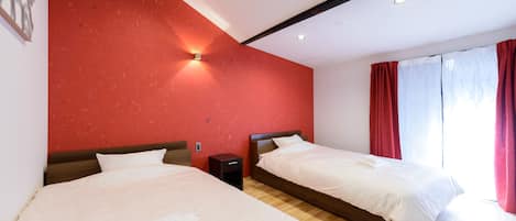 A hotel room with two beds, a red textured wall, a wooden headboard, a bedside table, and a window with red curtains.