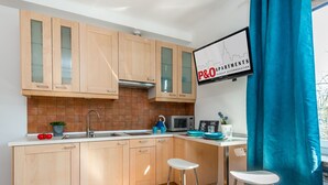Une cuisine moderne avec des meubles en bois, un four à micro-ondes et un évier. On y trouve deux tabourets et une fenêtre avec un rideau.