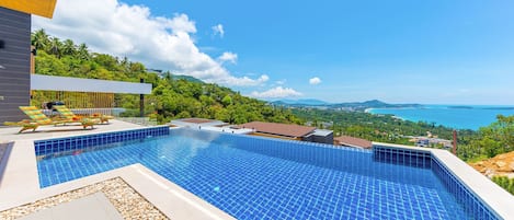 A swimming pool with a view of the sea and hills.