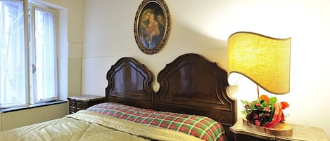 A bedroom with a bed, a nightstand, a lamp, a framed picture, and a window with curtains.