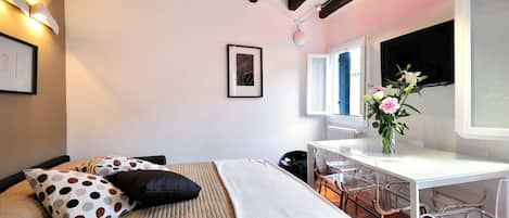 A bedroom with a bed, a desk, and a chair. There is a window with a view of the outside.