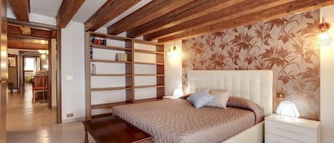 A bedroom with a bed, bedside tables, a nightstand, a wooden bench, and a bookshelf.