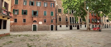 A courtyard with a paved ground, a tree, and a building with multiple windows and balconies.