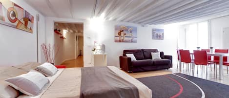 A modern hotel room with a bed, a sofa, a dining area, and artwork on the walls.