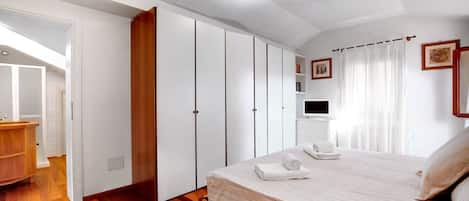 A bedroom with a bed, a television, a wardrobe, and a bathroom.