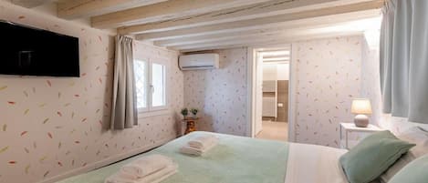 A bedroom with a bed, a TV mounted on the wall, and a window with curtains.
