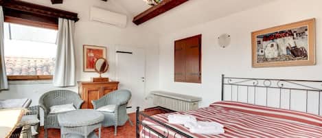A room with a bed, wicker chairs, a desk, and a radiator.