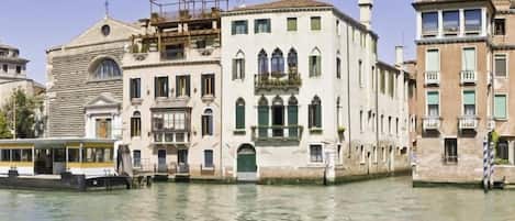 Un edificio histórico con un canal de agua en primer plano, una embarcación amarrada al canal, y otro edificio con un balcón.