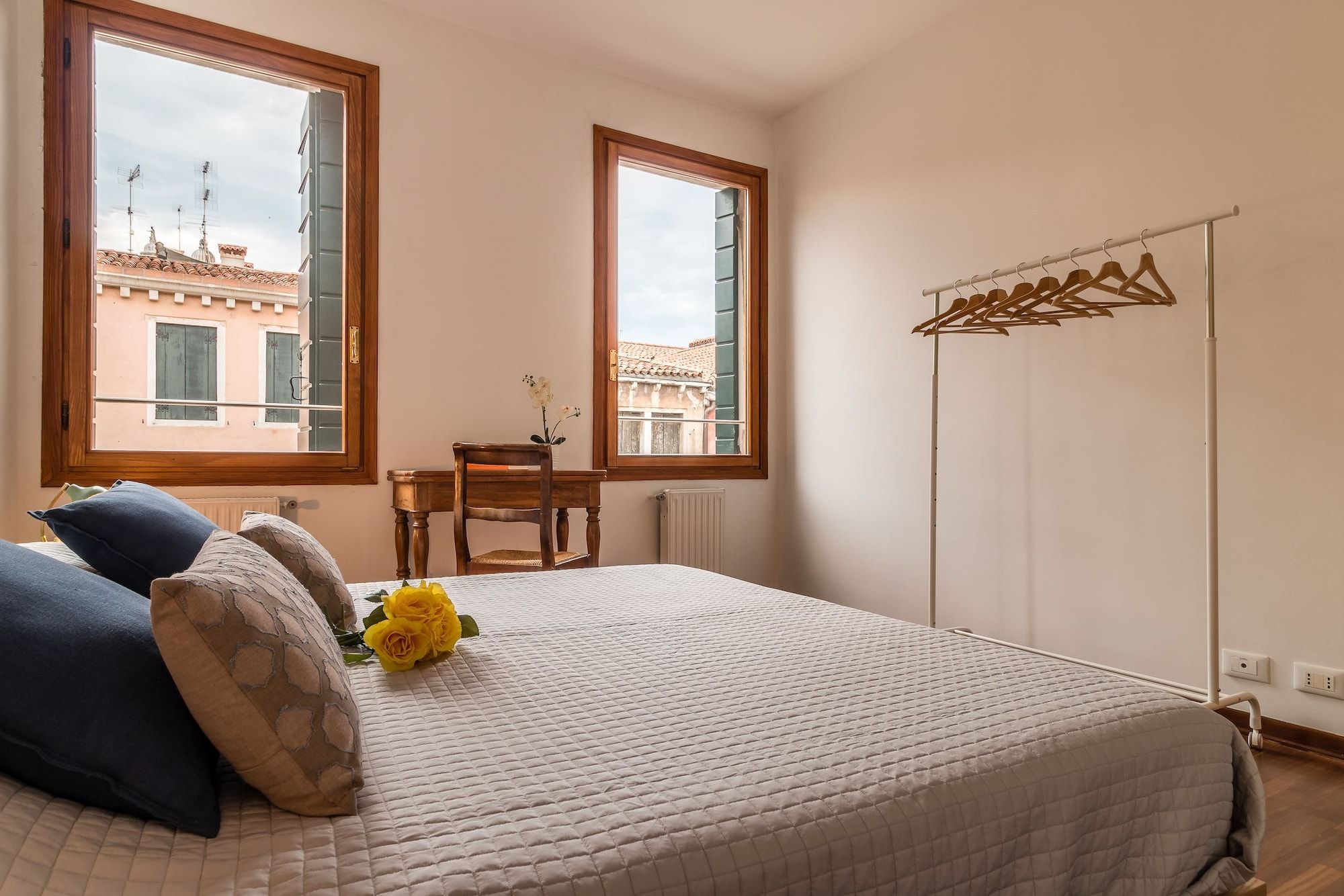 Quarto com cama, duas janelas, uma cadeira e um radiador.