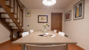 A dining area with a wooden table, chairs, a vase with flowers, and framed artwork on the walls.