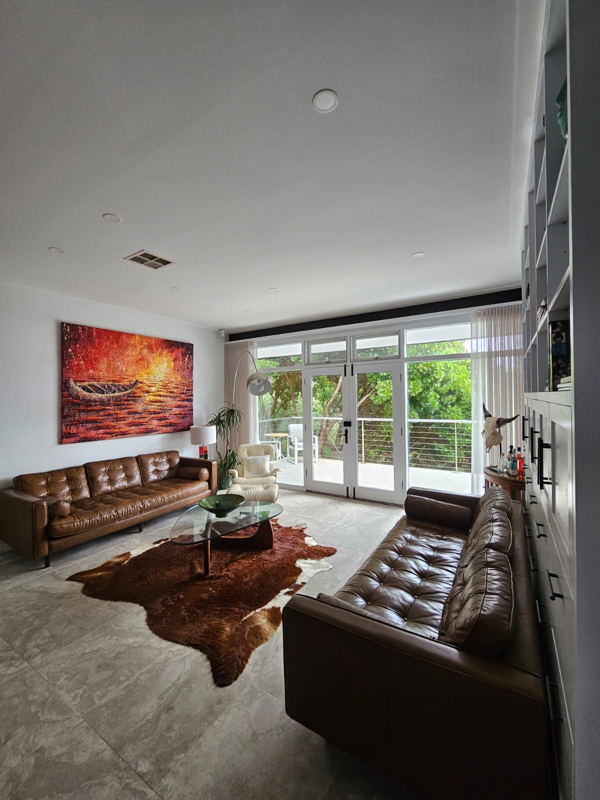 A modern living room with a leather sofa, a glass coffee table, and a large painting.