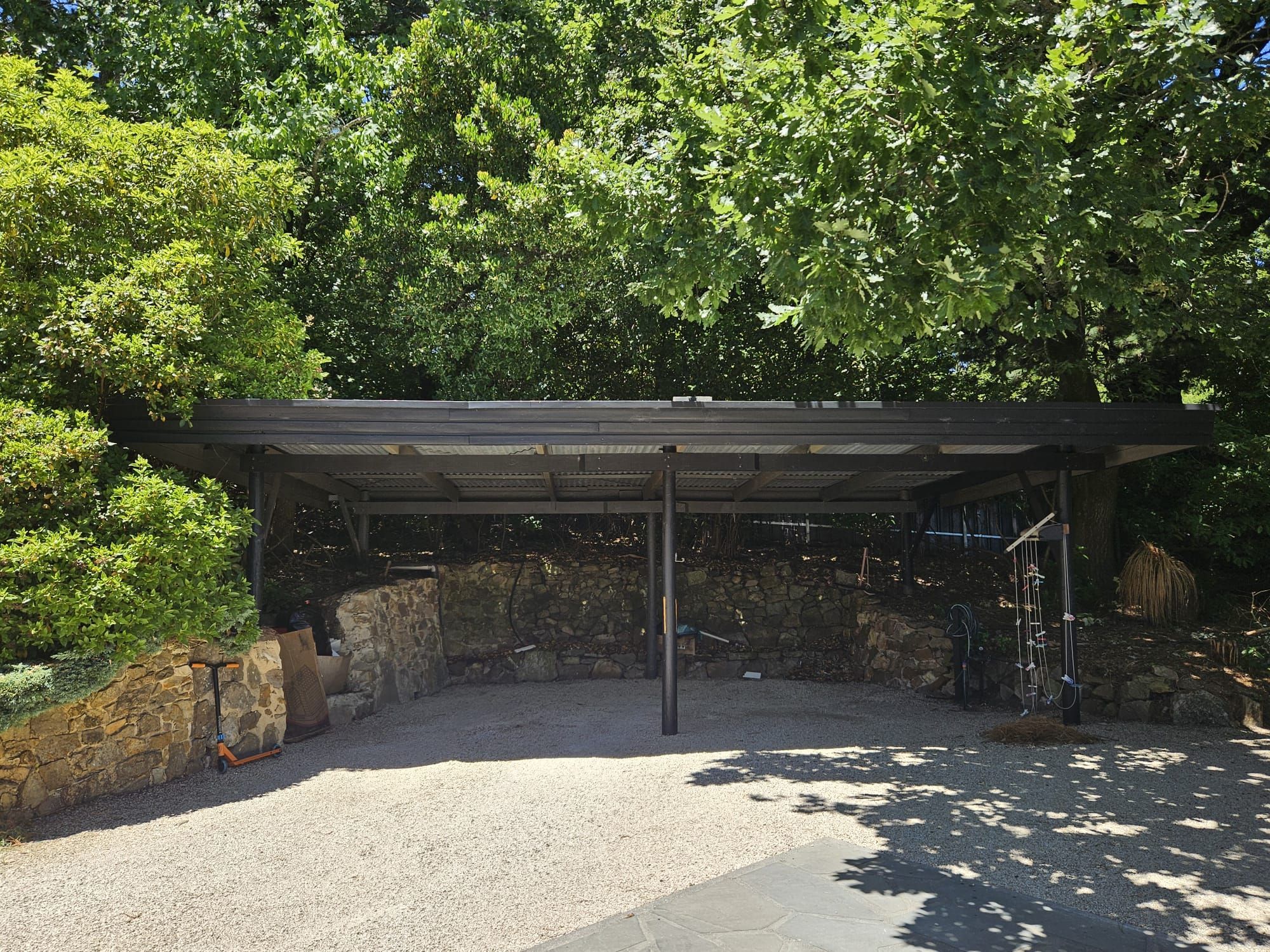 A covered outdoor area with a gravel floor, surrounded by stone walls and dense foliage.